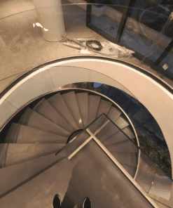 Escada helicoidal com guarda corpo de vidro curvo executada por Escadas Especiais em um ambiente hall de entrada principal de uma edifício residencial