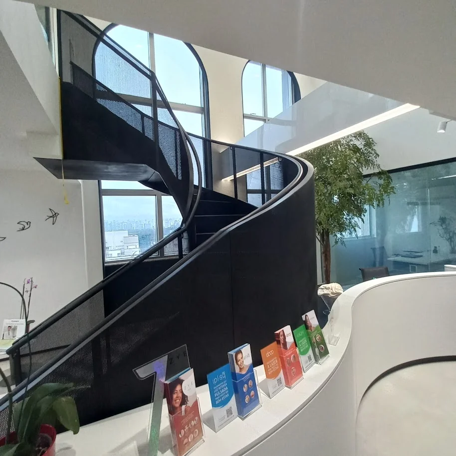 Vista lateral completa de escada helicoidal metálica preta em espaço de saúde premium com recepção branca