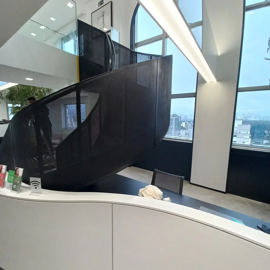 Escada helicoidal metálica preta em recepção de espaço de saúde de alto padrão com skyline de São Paulo ao fundo
