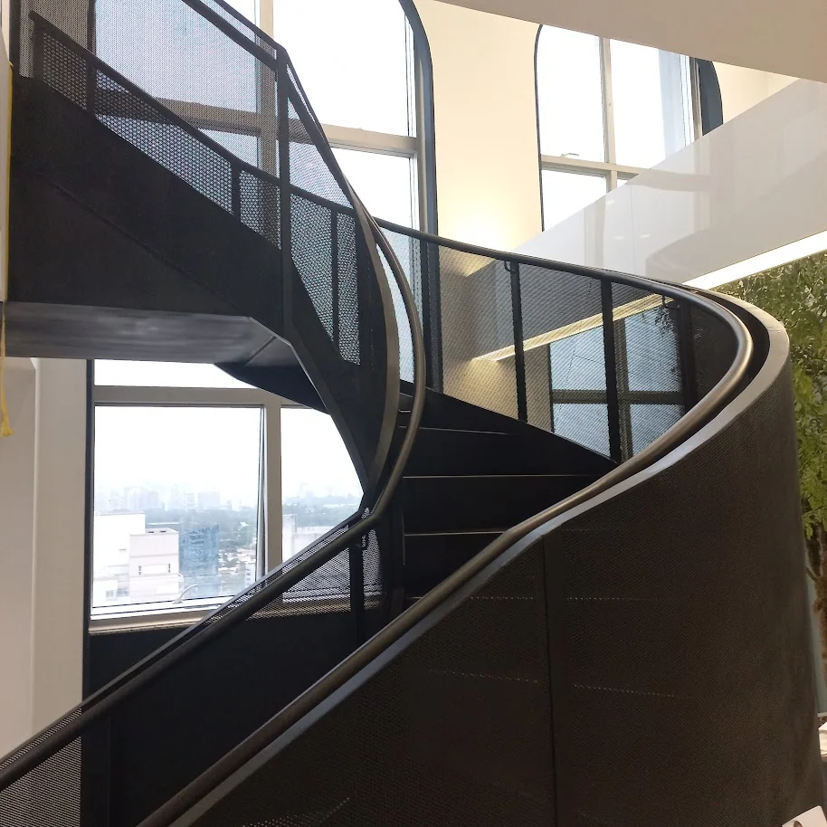Detalhe da chapa metálica perfurada de escada helicoidal preta com luz natural e paisagem urbana de São Paulo